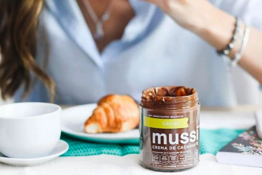 Frasco de mussi Cacao en una mesa con café y croissant